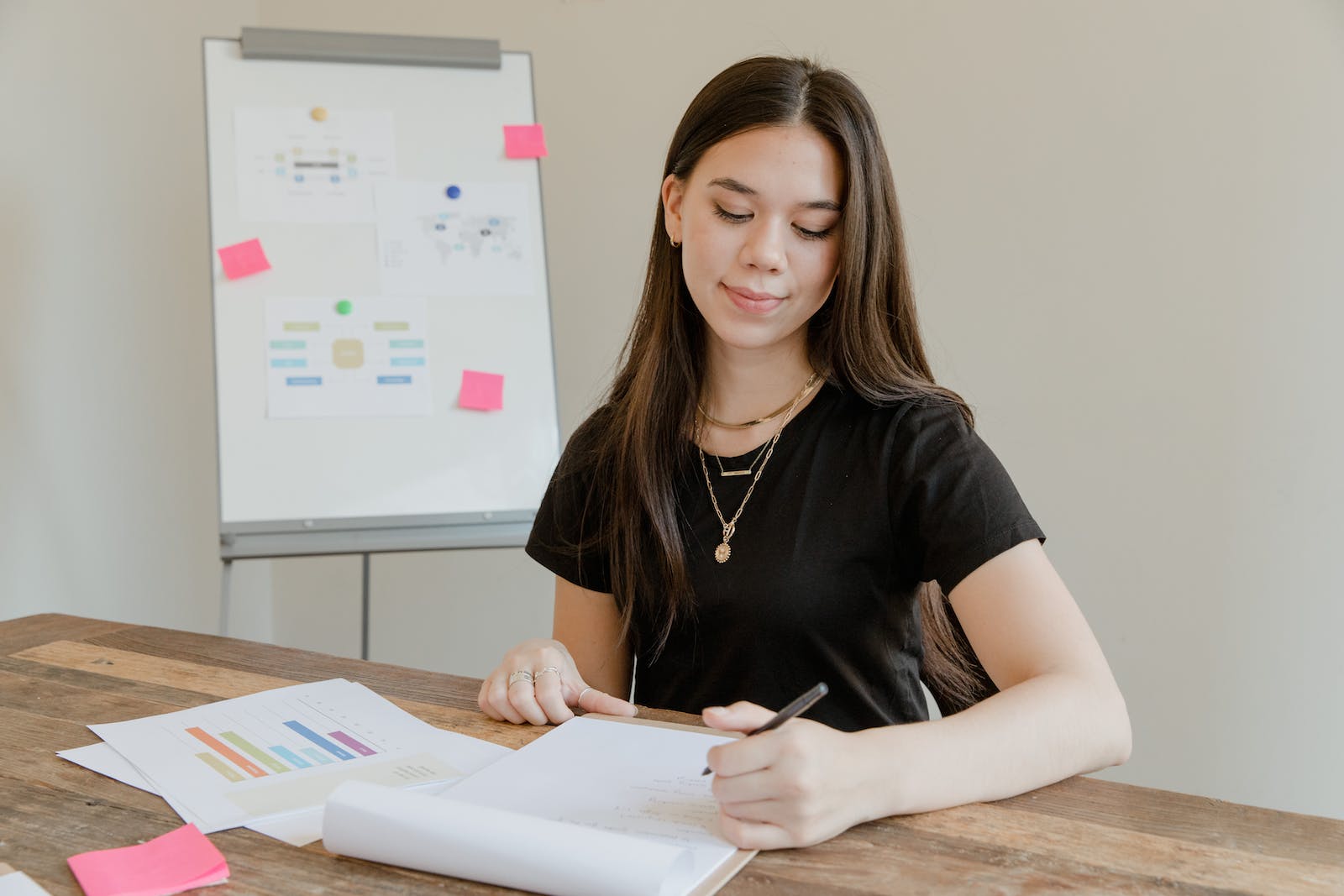A Woman in Black T-shirt Near Wooden Table Holding a Pen Over a Paper